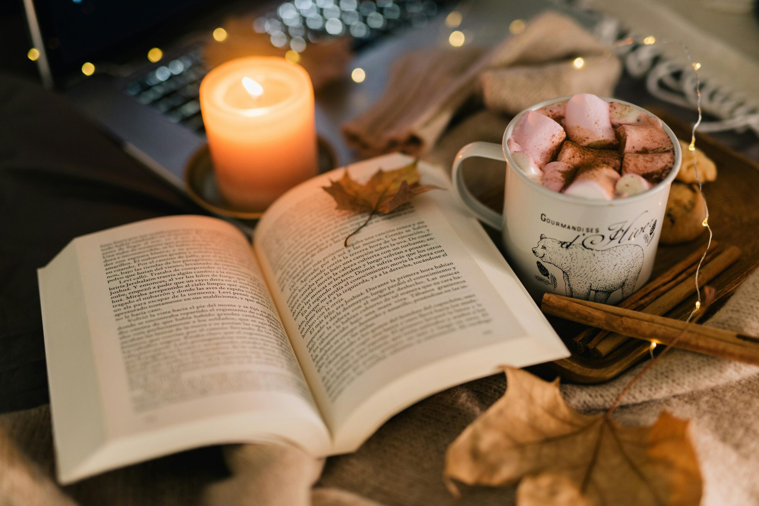 A warm evening scene with an open book, a candle, and a cup of hot chocolate topped with marshmallows — symbolizing a peaceful, phone-free hour before bed.