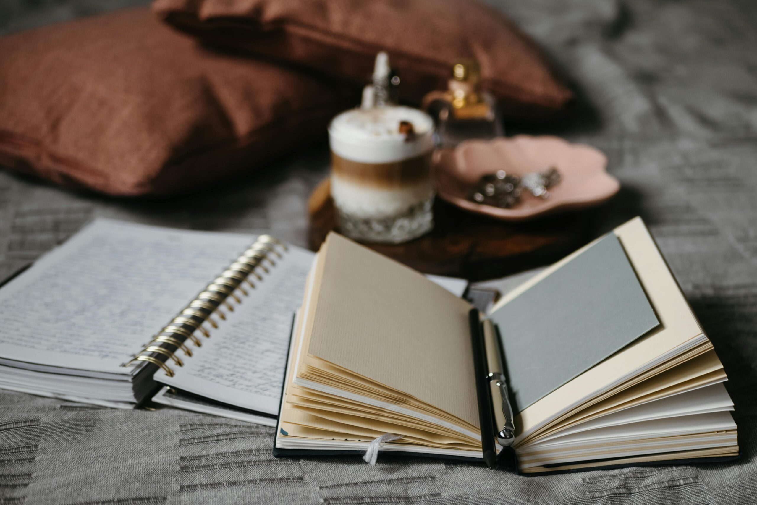 Open journal and notebook with coffee and soft pillows in warm light — calm slow living and journaling scene for a reflective Sunday moment.