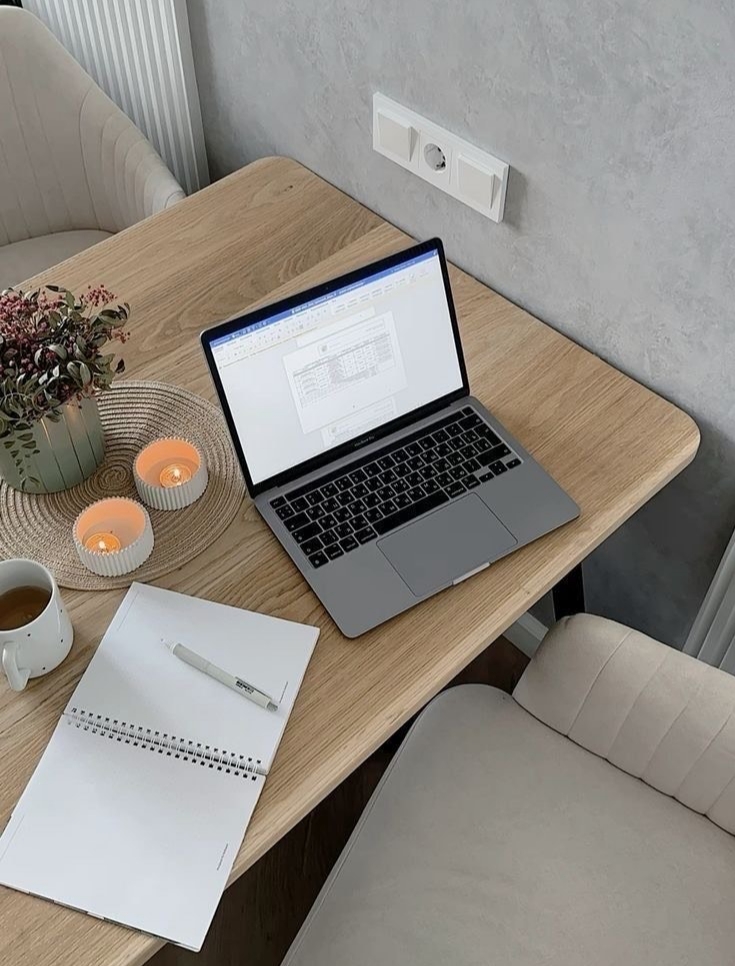A soft, neutral office desk with an open laptop, a notebook, a cup of coffee and two small candles. Warm light, beige tones and a quiet workday atmosphere that reflects gentle boundaries and office fatigue.