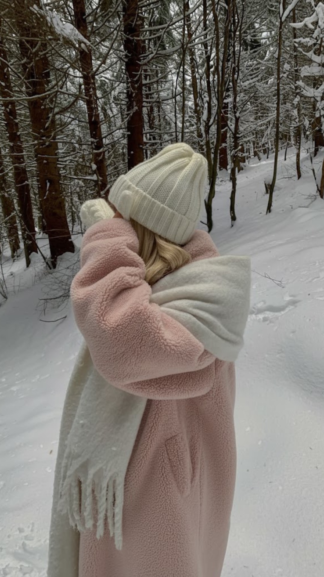 Woman in a soft blush winter coat and white scarf walking alone in a quiet snowy forest, capturing the calm, introspective mood of a 7-day quiet confidence challenge.