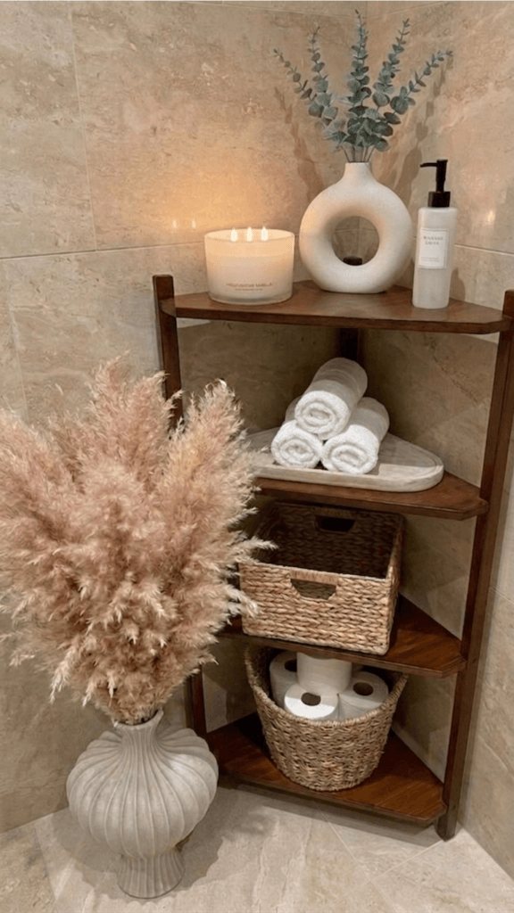  small bathroom corner shelf styling with wooden 4 tier shelf, rolled white towels, woven baskets, candle and neutral decor to reduce visual clutter