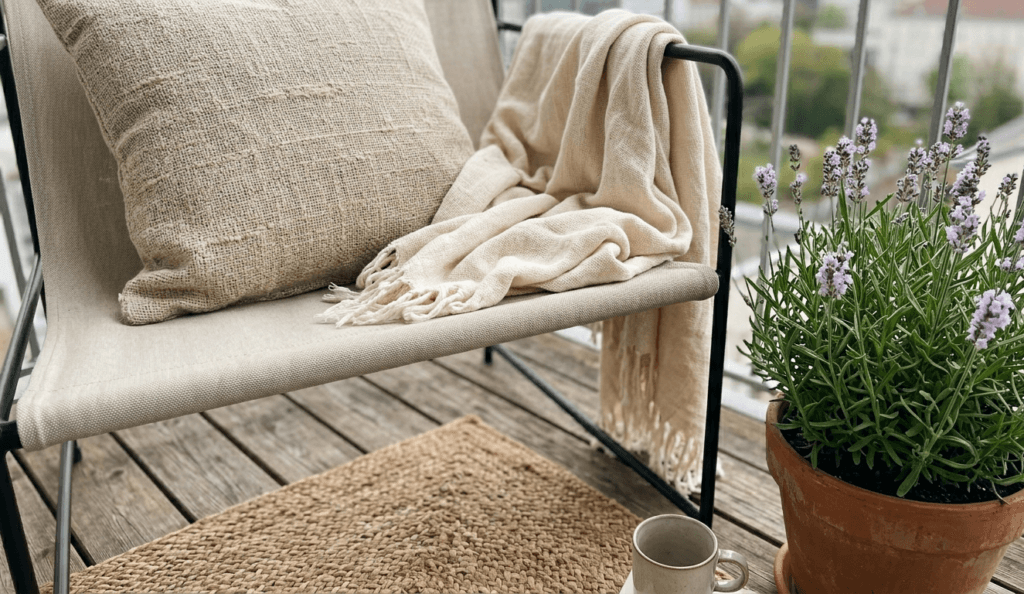 cozy balcony corner with soft cushion, throw blanket and lavender plant, warm textures and relaxing outdoor seating detail