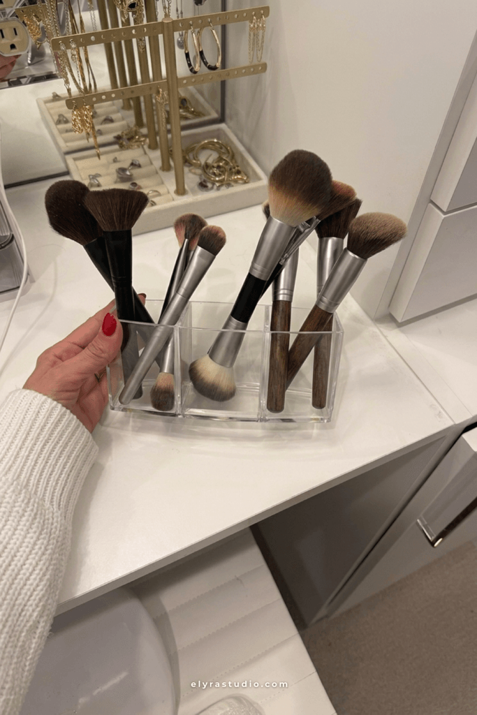 Clear acrylic makeup brush holder organizing face and eye brushes on a clean white vanity countertop