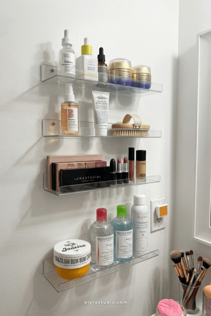 Clear acrylic floating wall shelves organizing skincare, makeup, perfume, and beauty products above a small vanity setup