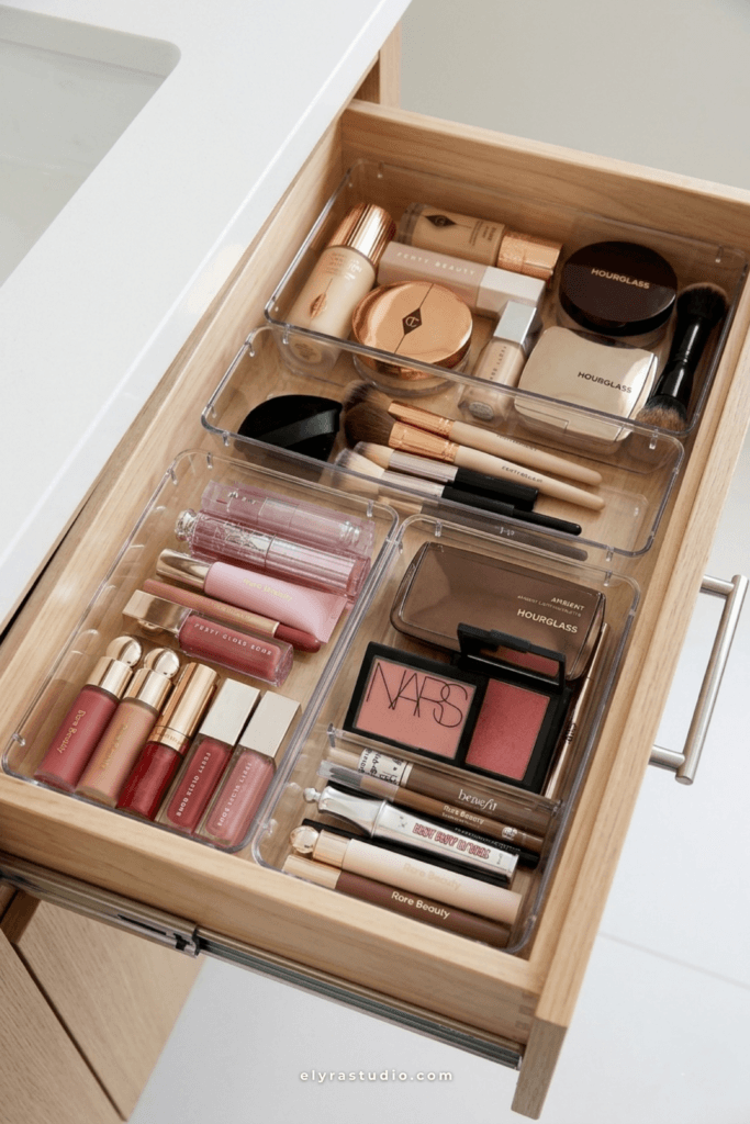 Clear acrylic makeup drawer organizers with foundation, blush, lip gloss, and makeup brushes neatly organized inside a wooden vanity drawer